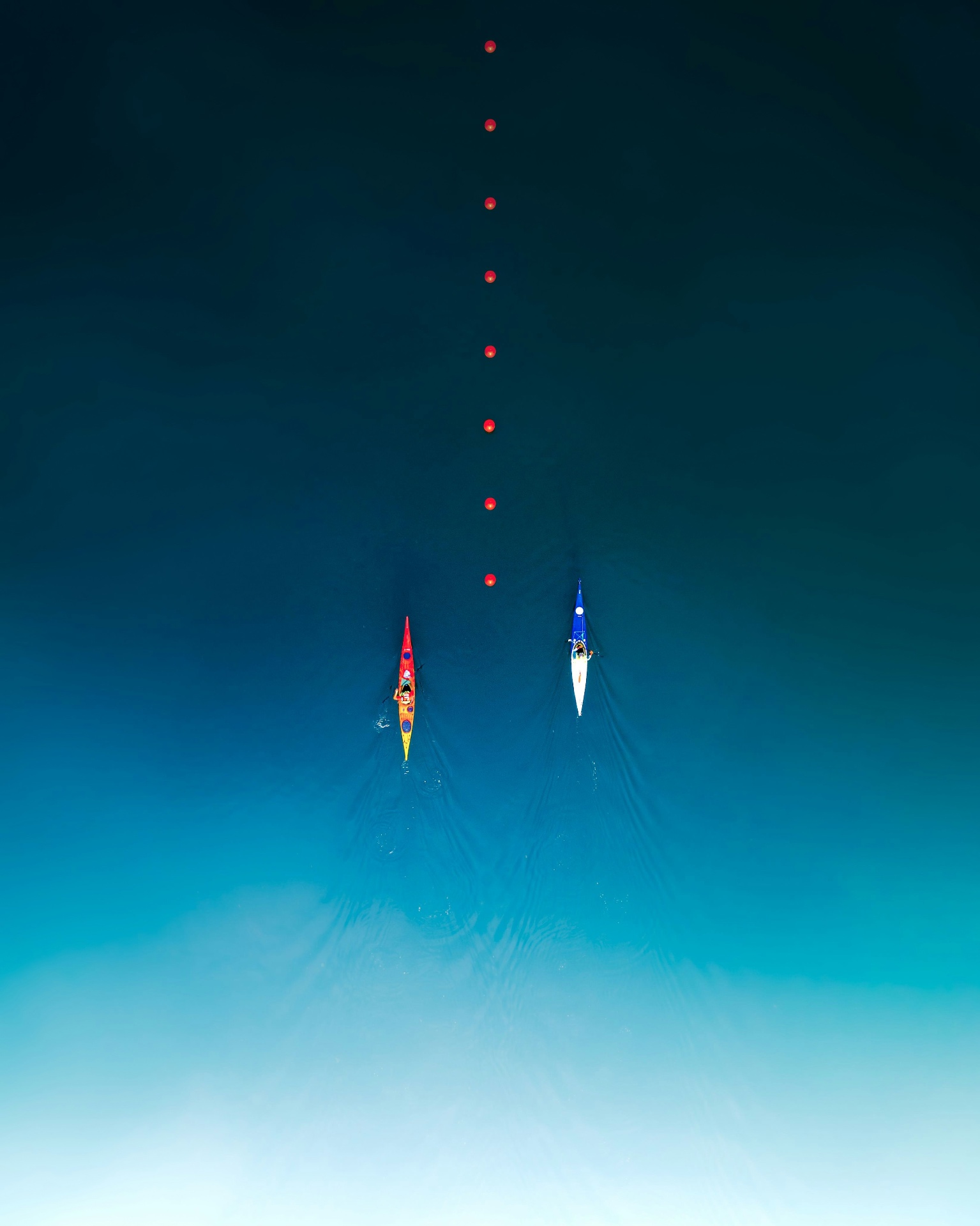 Two kayaks tracing parallel lines through deep water past a row of buoys